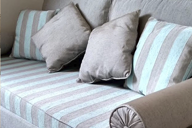 cama transformada em sofá, 2 encostos em cinza brilhante, 2 almofadas decorativas listradas e 2 lisas, colchão com capa listrada de azul e cinza, rolinho com botão na lateral e base da cama com capa cinza 