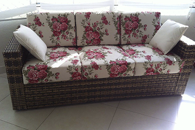 Sofá de vime de três lugares de almofadas com capa em tecido floral e duas almofadas decorativas laterais em tecido cru